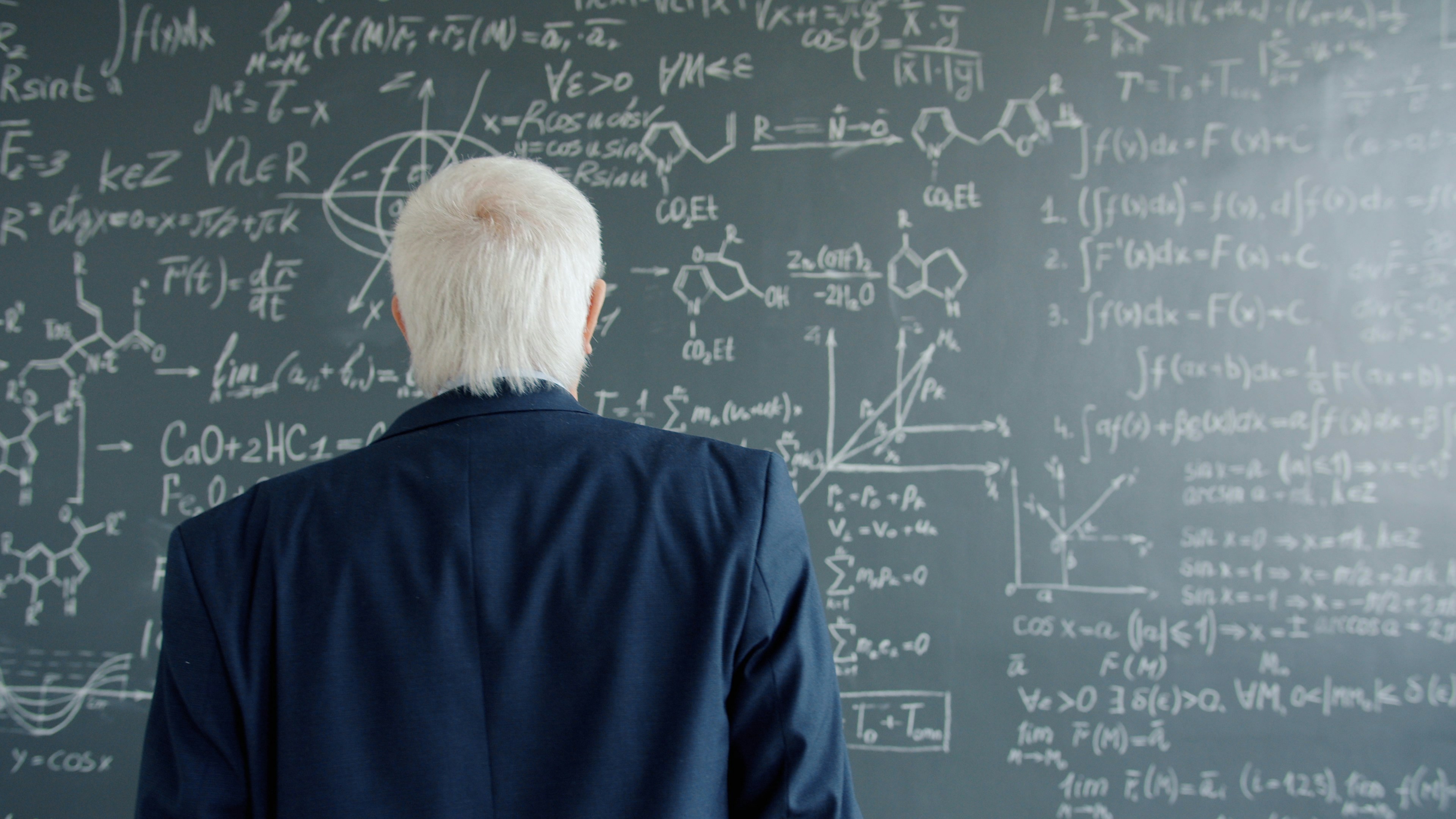Professor studying complex equations on a chalkboard